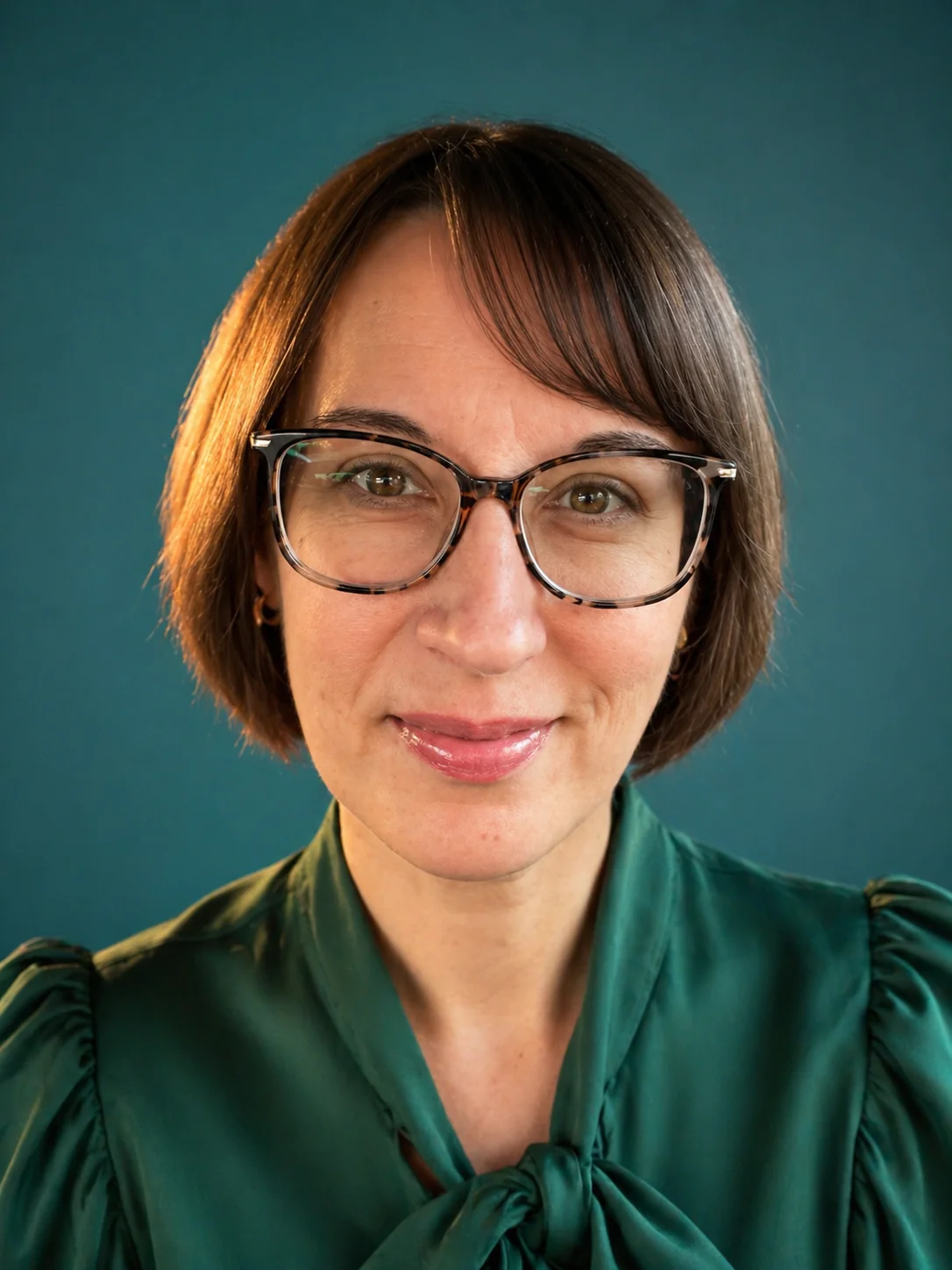 Erin Andress, a woman with shoulder-length brown hair and tortoiseshell glasses smiles at the camera, wearing a dark green blouse.