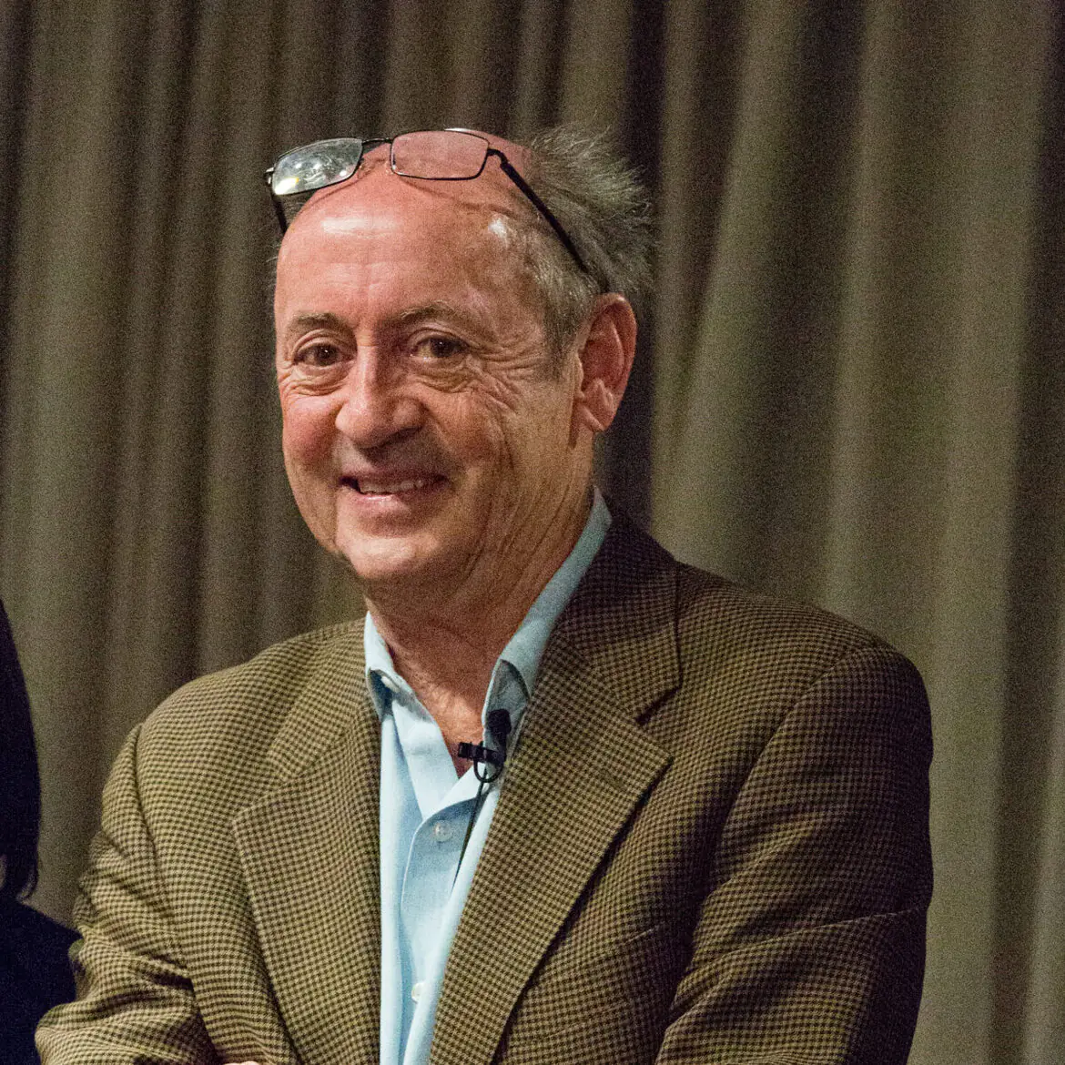 A smiling middle-aged man and Central Florida nonprofit leader wearing a light blue button-down shirt and a patterned blazer, with glasses resting on top of his head.