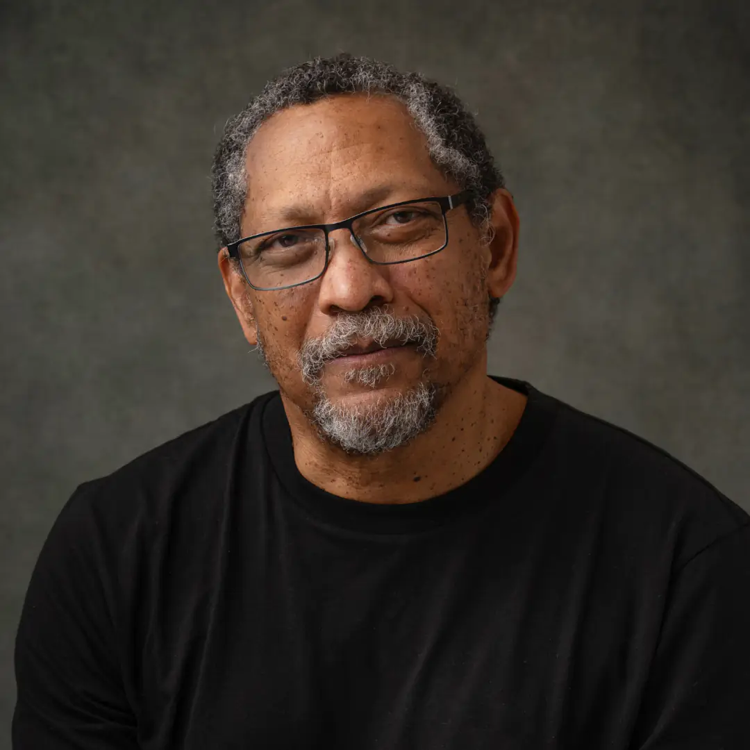 A portrait of a middle-aged man with a graying beard and glasses wearing a black t-shirt.