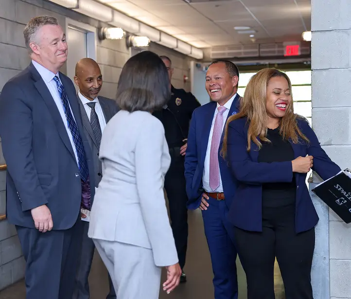 Guests in business attire smiling and greeting one another in a hallway.