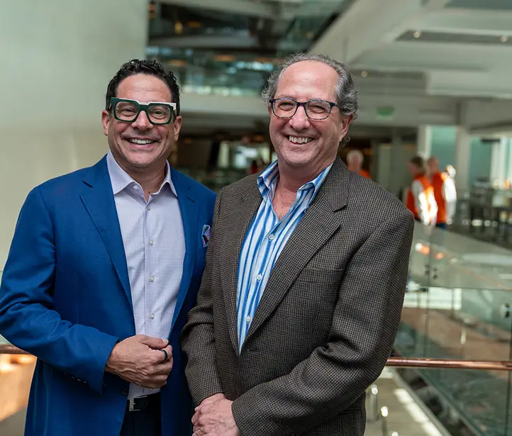 Two men in suit jackets smiling together in a bright indoor atrium.