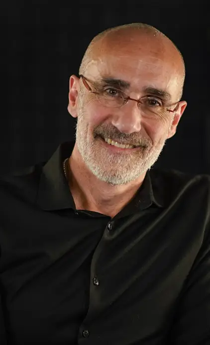 Portrait of a smiling man with glasses and a white beard wearing a black shirt.