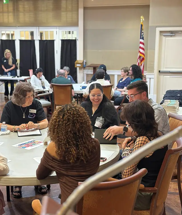 Younger and older adults sharing a discussion around tables with books and notebooks.