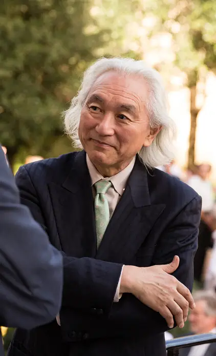 A man with shoulder-length white hair wearing a dark suit and light green tie outdoors.