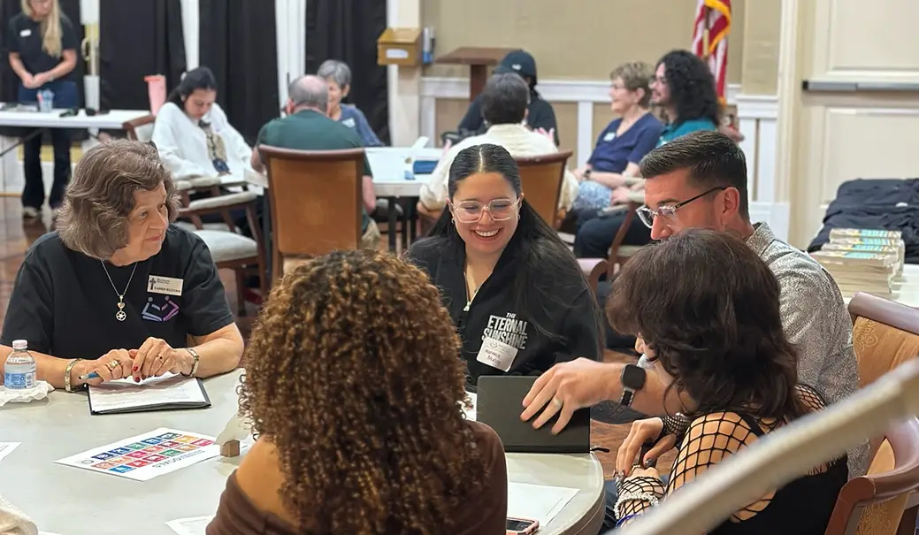 Younger and older adults sharing a discussion around tables with books and notebooks.