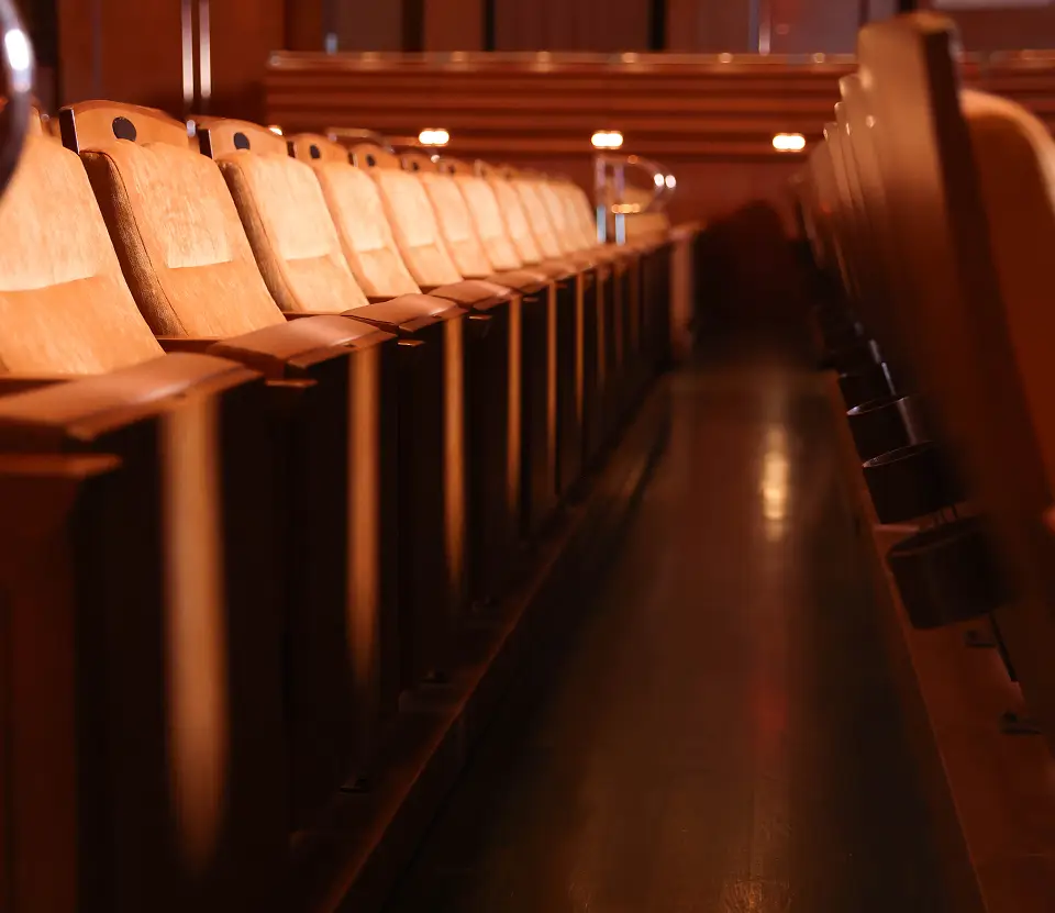 Rows of empty wooden seats lining an aisle in an auditorium.