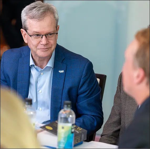 A man in glasses and a blue jacket listening during a small-group discussion.