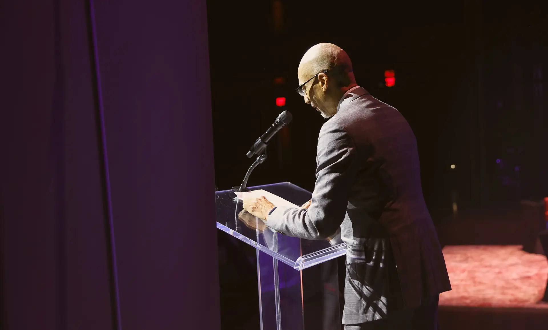 A speaker addressing the audience from a clear lectern on a theater stage.