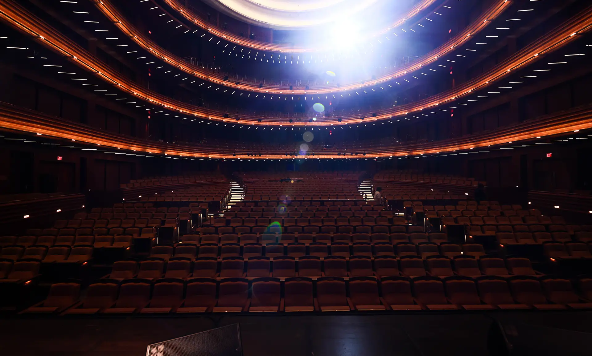 Rows of seats and curved balconies in an empty theater, viewed from the stage.
