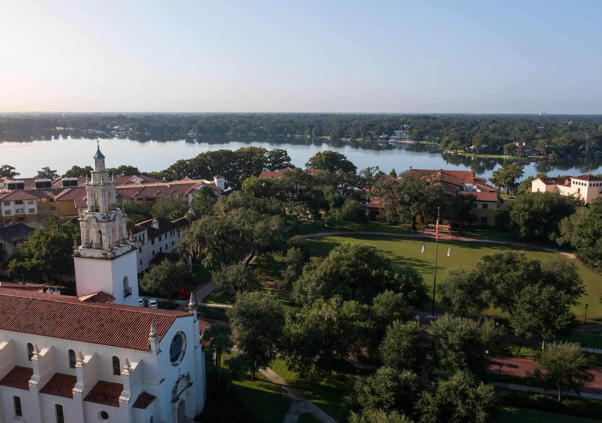 Aerial view of a Central Florida nonprofit campus featuring a white chapel, a large green lawn with a flagpole, and a lake in the background.