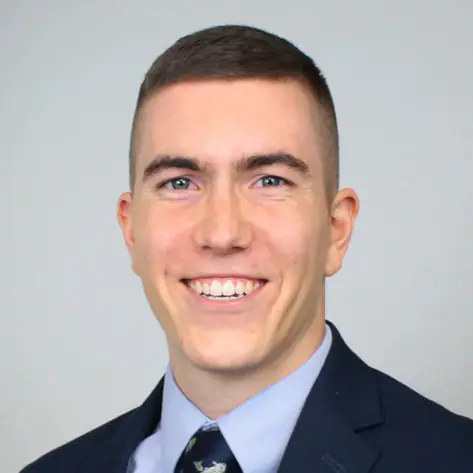 Headshot of Caleb Liptak, a smiling man wearing a dark suit, light blue dress shirt, and patterned tie.