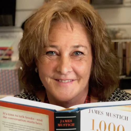 A smiling woman from a Central Florida nonprofit holds an open copy of the book 1,000 Books to Read Before You Die by James Mustich.