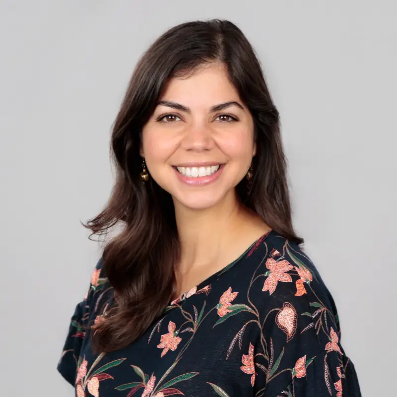 Megan Almasi, a woman with shoulder-length dark hair, smiling at the camera and wearing a dark floral top.