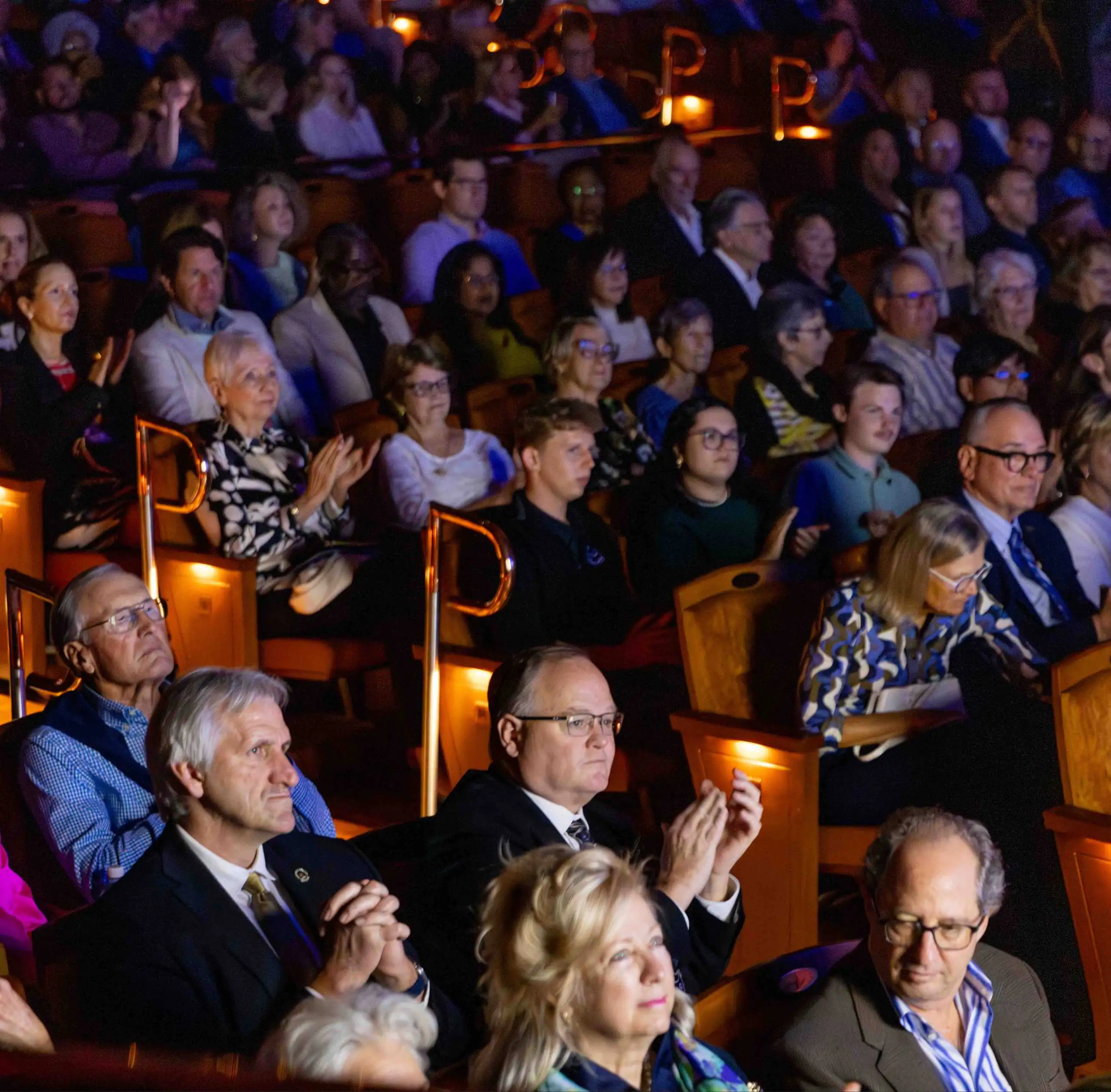 An audience seated in a darkened Winter Park Institute theater, with several people in the foreground clapping.
